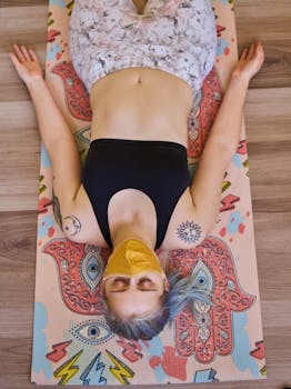 Woman in sports bra with tattoos doing yoga in Shavasana pose, eyes closed, wearing face mask.
