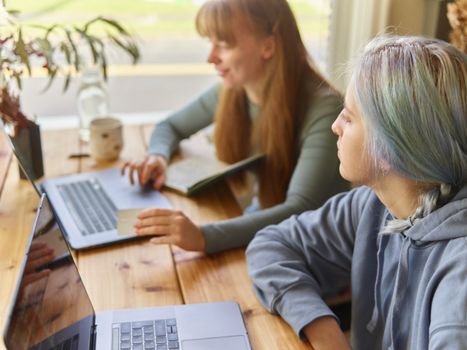 Two women working together with laptops in a bright indoor setting, fostering creativity and teamwork.