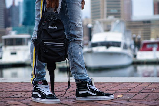 A close-up of a trendy urban outfit featuring black sneakers and blue jeans by the marina in Baltimore.