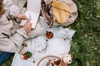 Person Holding White Box Near Brown Leather Bag and White Ceramic Mug on Green Grass