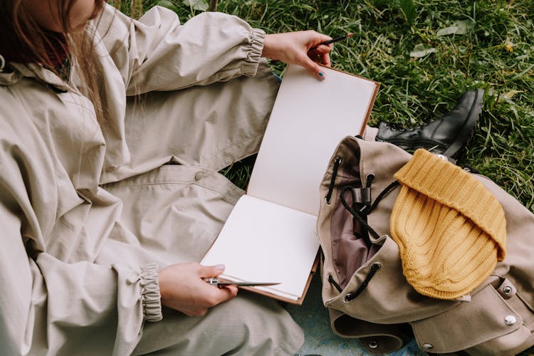 Woman Sitting On The Grass With An Open Scrapbook 