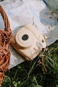 A beige Polaroid camera placed on a map outdoors, surrounded by grass and a wicker basket.