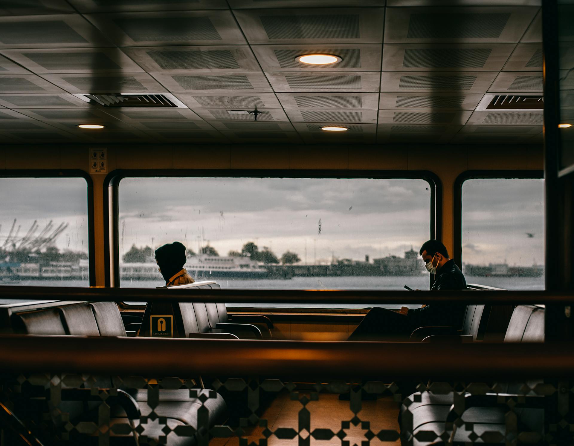 Passengers travel on an Istanbul ferry, enjoying views through large windows with the city in the background.