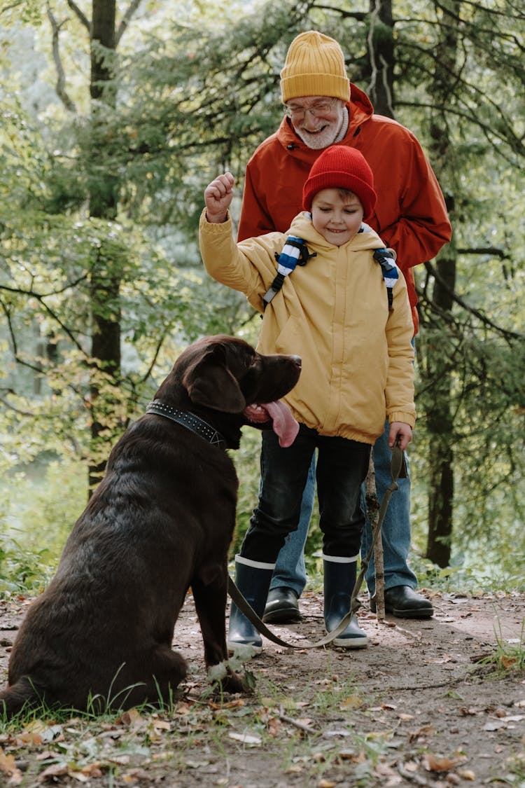 An Elderly Man And A Young Boy Standing Beside Their Pet Dog