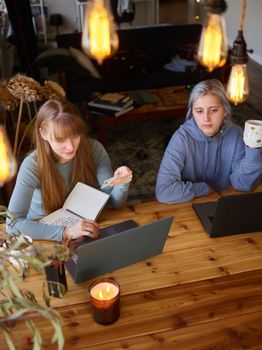 Two women at a wooden table engaged in online shopping, using laptops and holding a credit card.