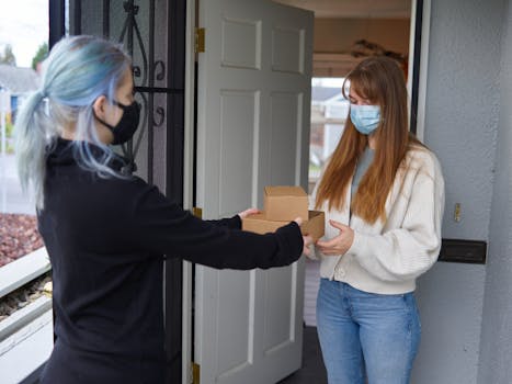 Two women with face masks exchanging parcels, depicting online shopping during the pandemic.