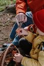 Child in Brown Jacket and Red Knit Cap Holding Brown and Black Dried Fish