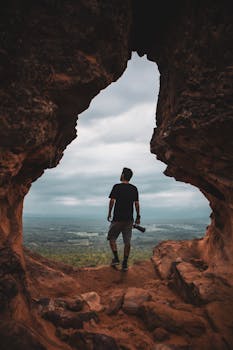 Silhouette of a man exploring a cave with a stunning view, capturing the essence of adventure and travel.