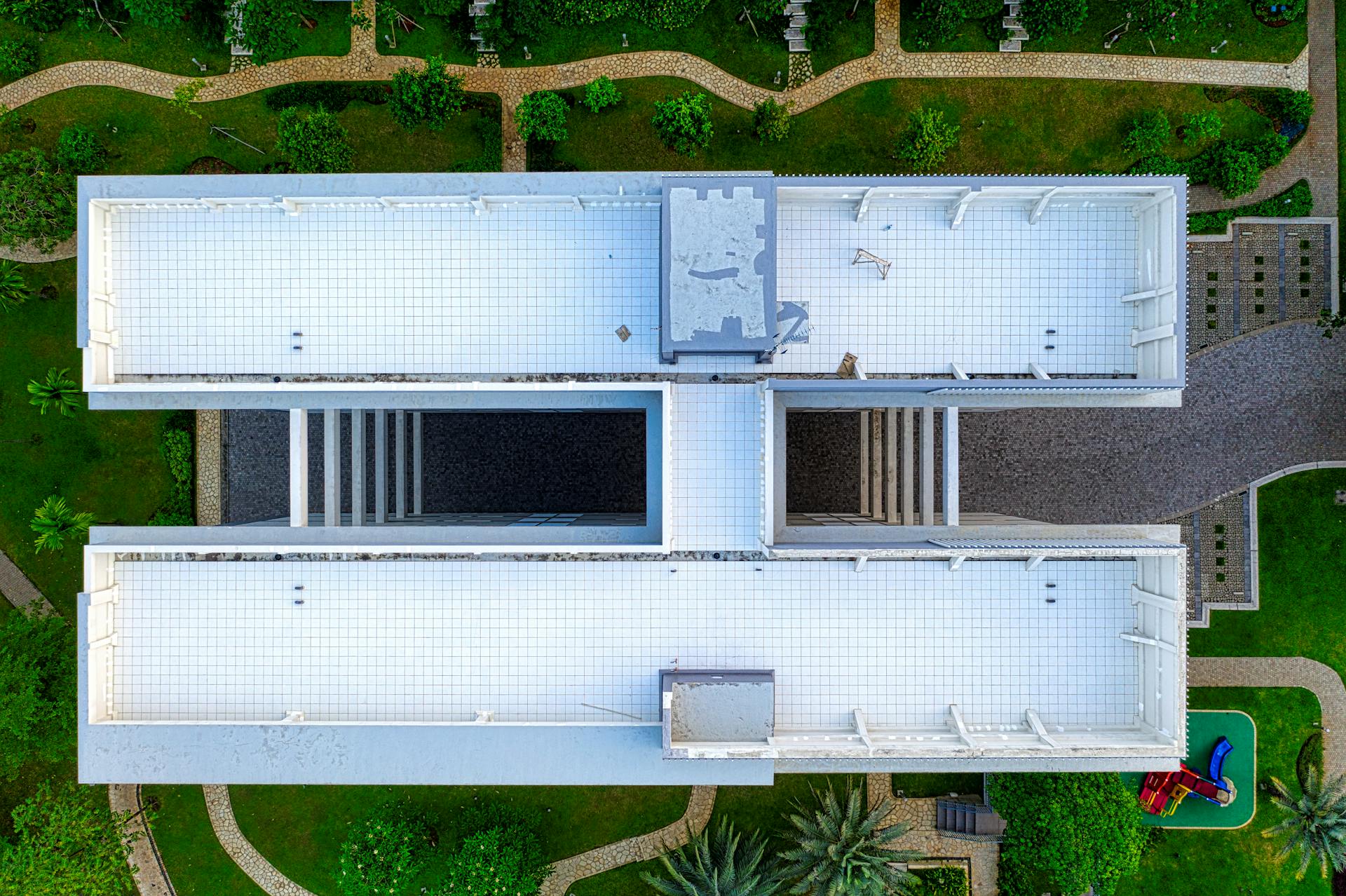 Drone view of roof of residential building placed among green grass and plants in town in daylight