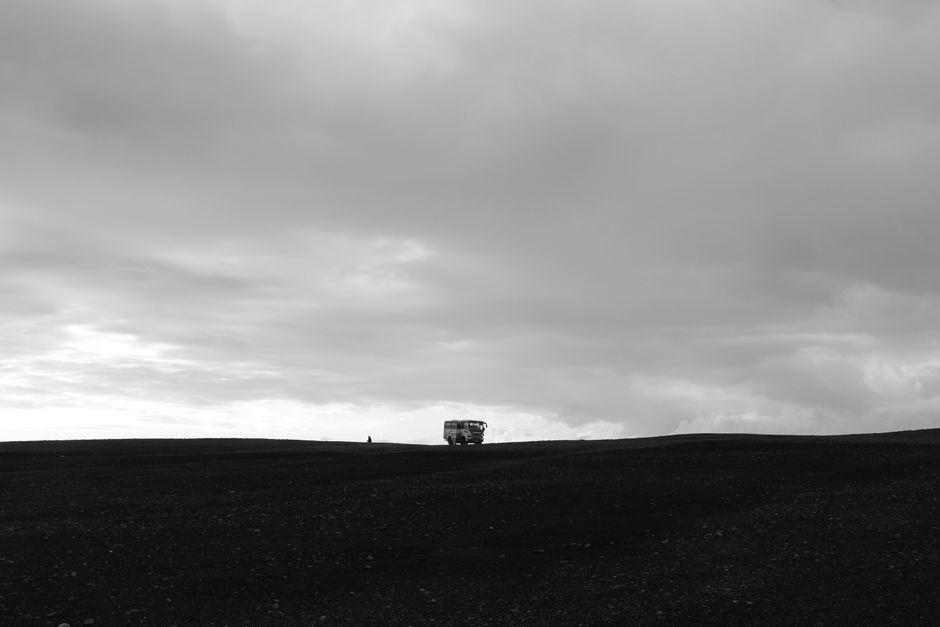 A van travels across the vast, dramatic Icelandic countryside under a cloudy sky.