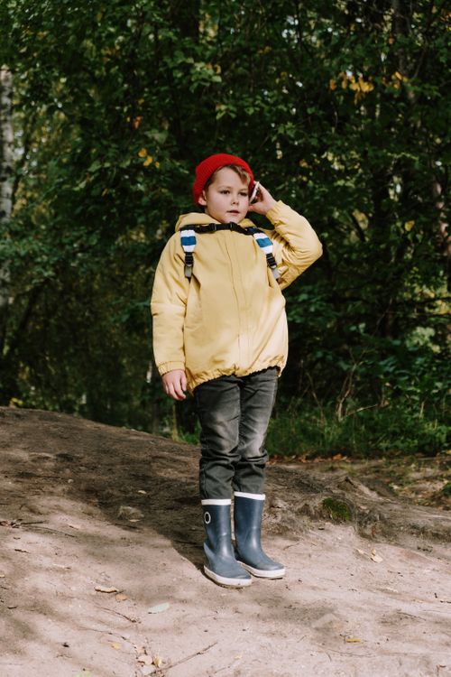 Free A young boy with a red hat explores a forest wearing a yellow jacket and boots. Stock Photo