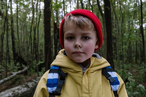 Free Portrait of a young boy in a forest wearing a red beanie and yellow jacket. Stock Photo