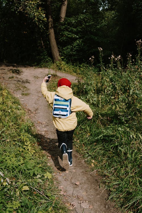 Junge Im Gelben Hoodie Und In Den Blauen Jeans, Die Auf Schmutzweg Zwischen Grünem Grasfeld Gehen