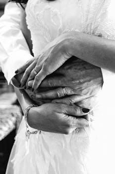 Intimate black and white photo of couple holding hands and embracing, showcasing love and connection.