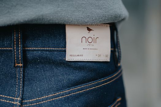 A detailed close-up of dark denim jeans with a brand label 'noir', captured in Jakarta.