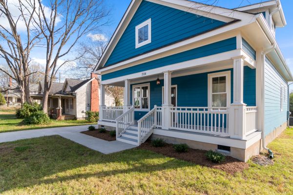 A cozy blue suburban house with a white front porch and lush surroundings