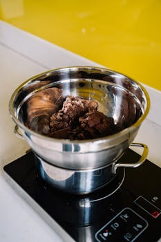 A stainless steel bowl with chocolate melting on an electric stove, ideal for culinary projects.
