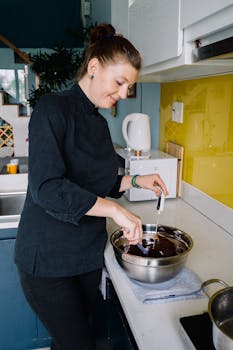 A female chef stirring melted chocolate in a modern kitchen, showcasing culinary skills.