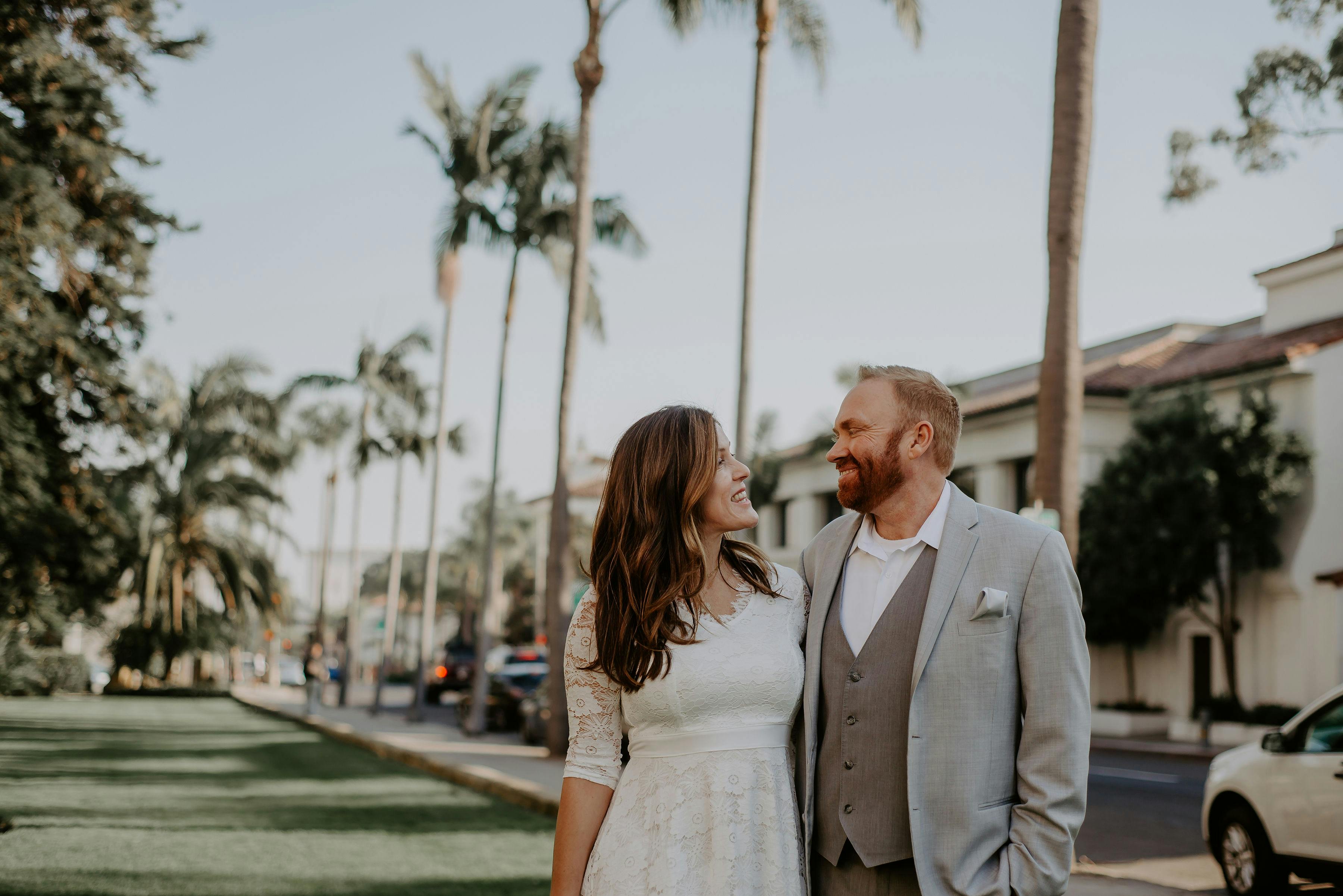 A joyful couple celebrates their wedding day outdoors with palm trees lining the street.