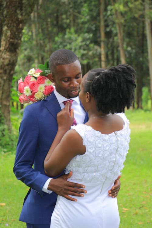 Free A bride and groom share an intimate embrace outdoors, holding a floral bouquet. Stock Photo