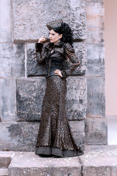A woman in a stylish steampunk costume poses against a stone wall, showcasing elegance and fashion.