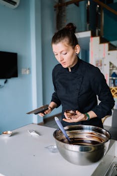 Woman in a black chef uniform preparing chocolate dessert indoors.
