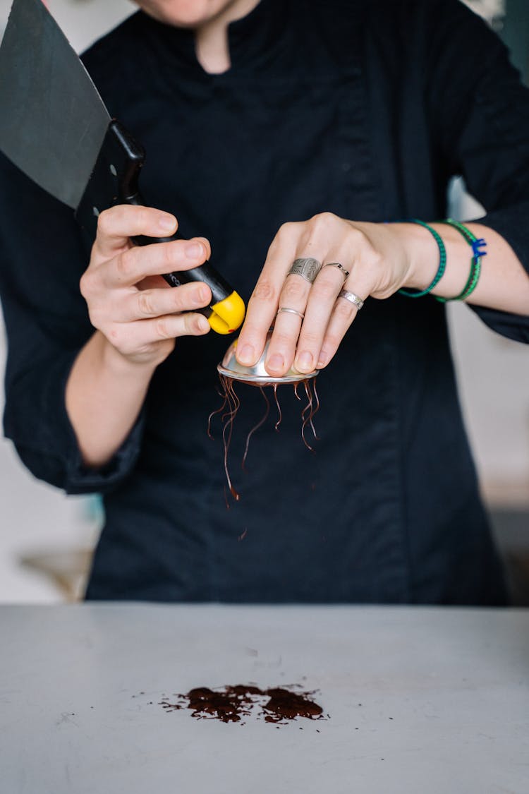 Hand Of A Person Holding A Metal Tool And A Small Container