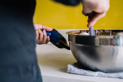 Person melts chocolate in a stainless steel bowl using a hair dryer for a unique cooking method.