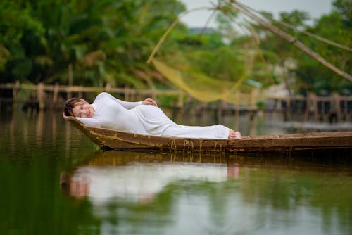 Woman in White Dress Lying on Brown Wooden Boat on Body of Water