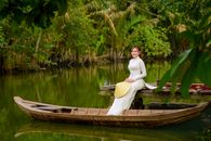 Woman in White Long Sleeve Shirt Sitting on Brown Wooden Boat on Lake