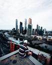 Man in White Red and Black Striped Shirt Sitting on the Edge of a Building Looking