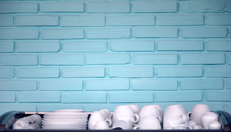 Fotomural Una pila de tazas y platos de cerámica blanca contra una pared moderna de ladrillos azules.
