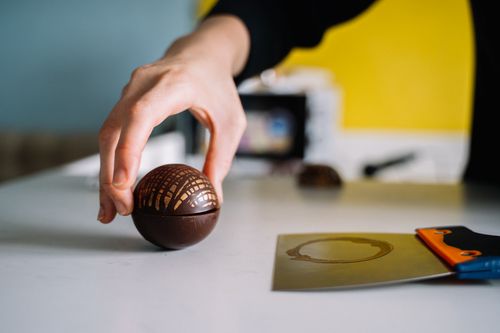 Free Close-up of a hand holding a decorative chocolate sphere with a scraper on the table. Stock Photo
