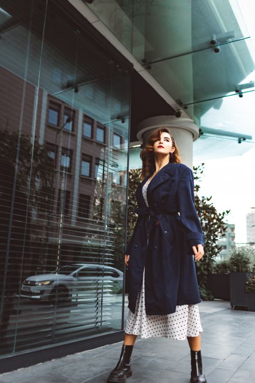 Free Elegant woman in a blue coat poses near a glass building in a cityscape, showcasing modern urban fashion. Stock Photo