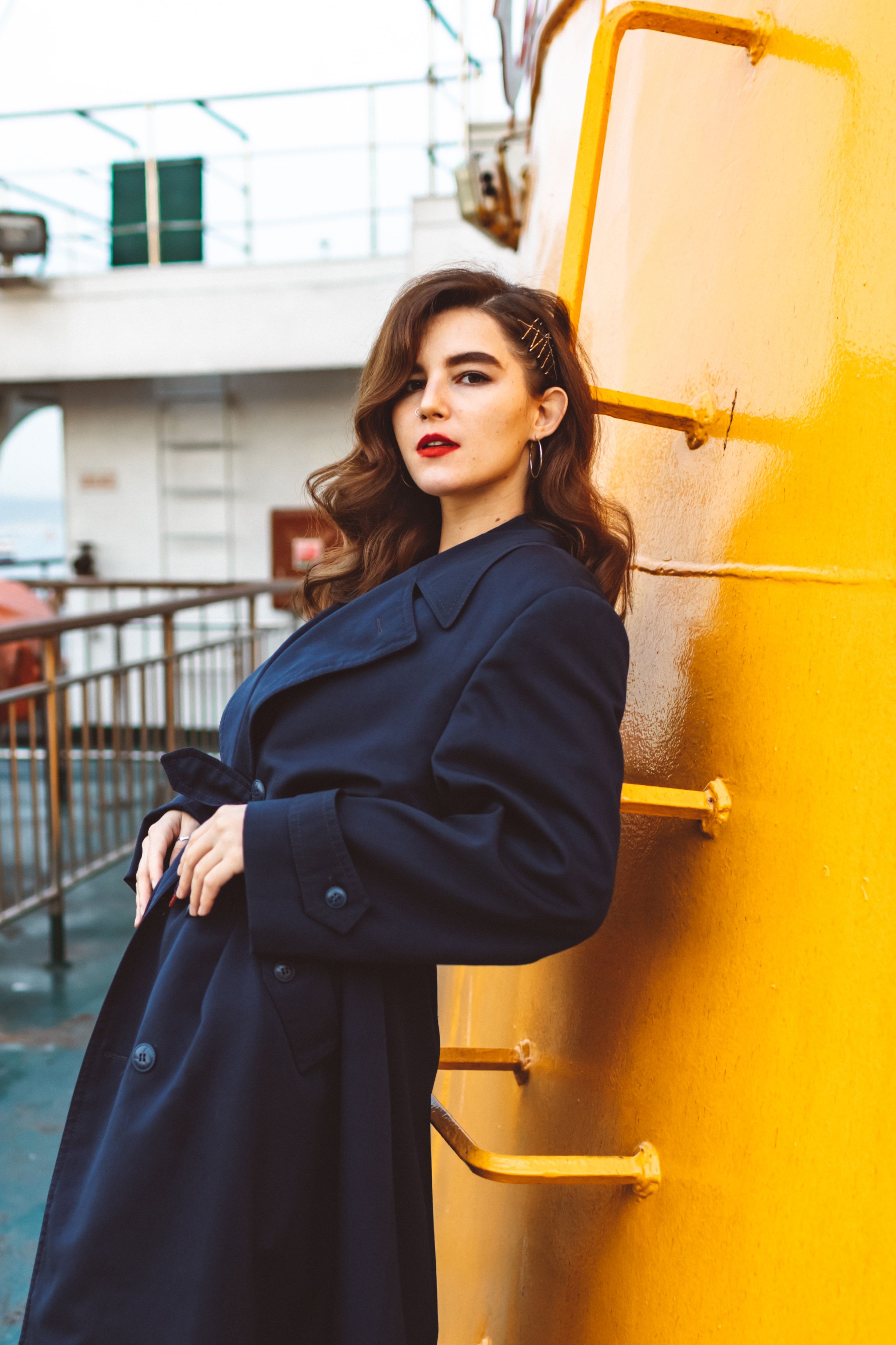 Fashionable woman in navy coat with makeup posing on a ship deck.