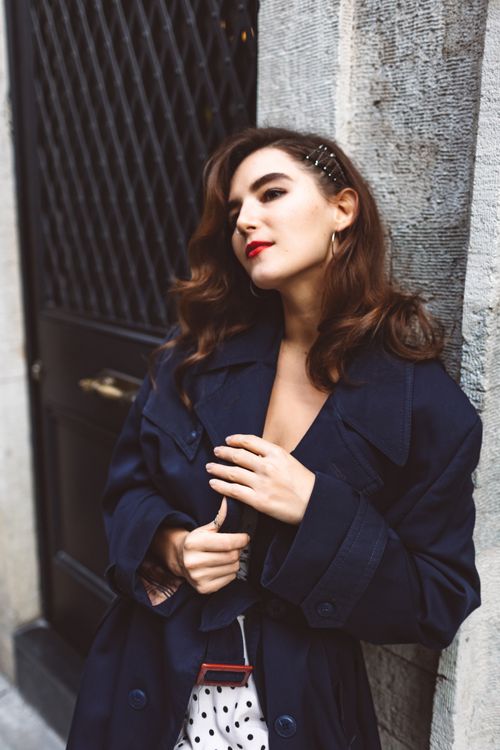 Free Portrait of a fashionable woman in a navy coat leaning against a textured wall Stock Photo