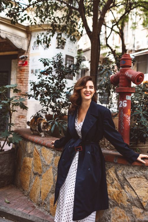 Free Young brunette woman in a polka dot dress smiling outdoors near a fire hydrant and trees. Stock Photo