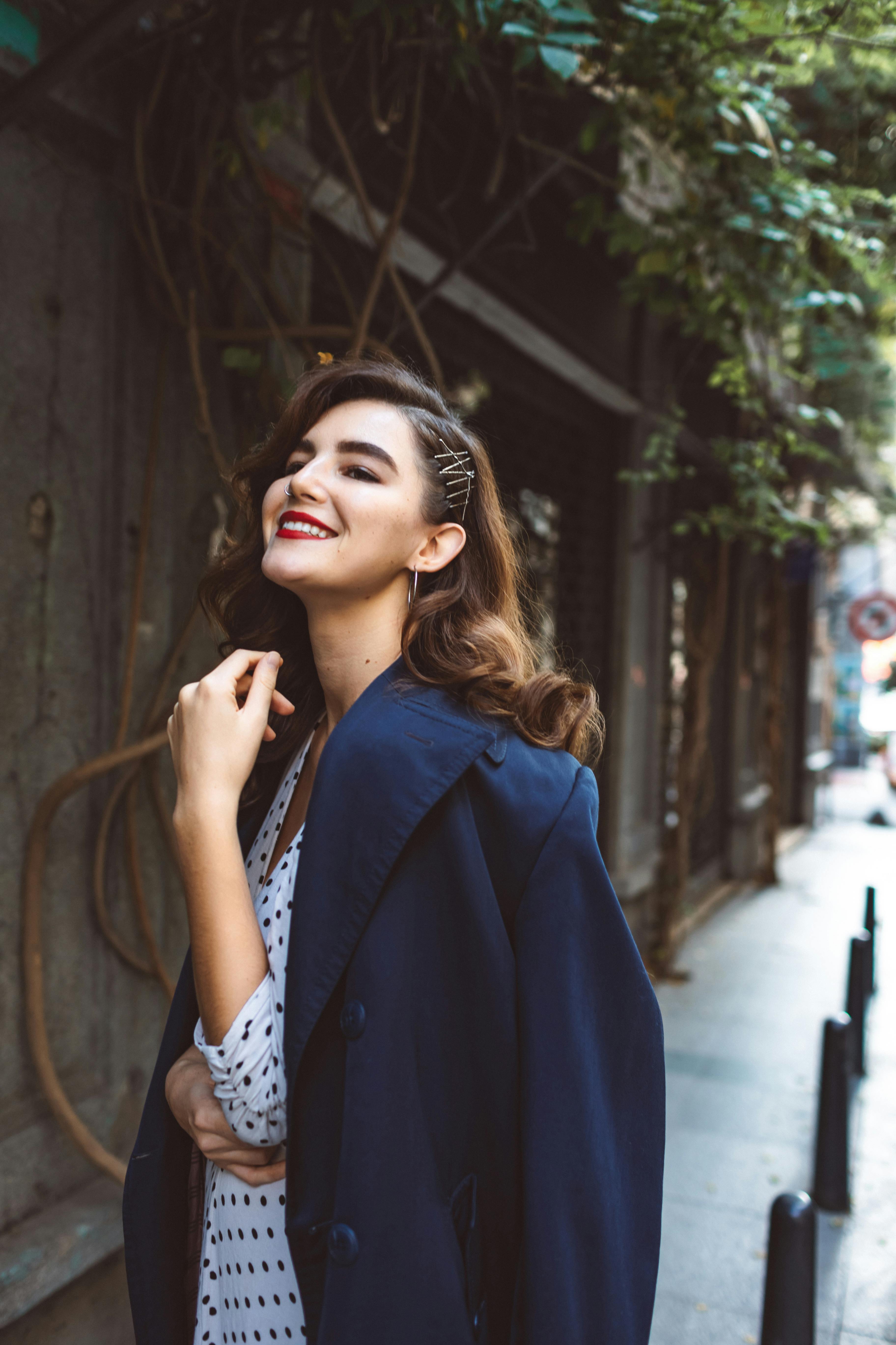 A fashionable woman smiles happily while posing in an urban setting, showcasing confidence and elegance.