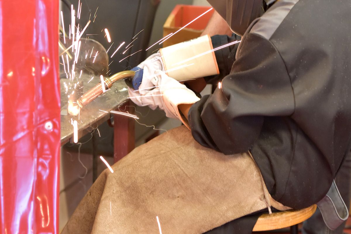 Femeie sudor la lucru, cu scântei care sar din piesa metalică prelucrată