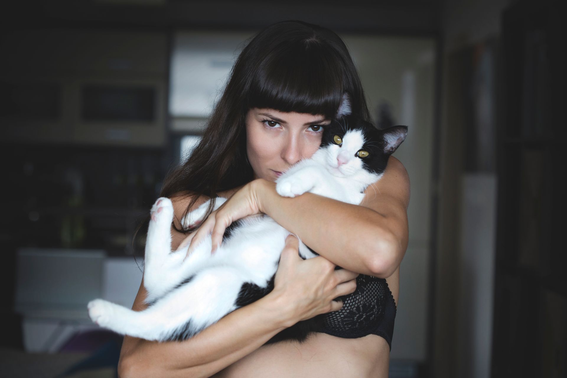 A woman lovingly cuddles her black and white cat indoors, showcasing warmth and companionship.