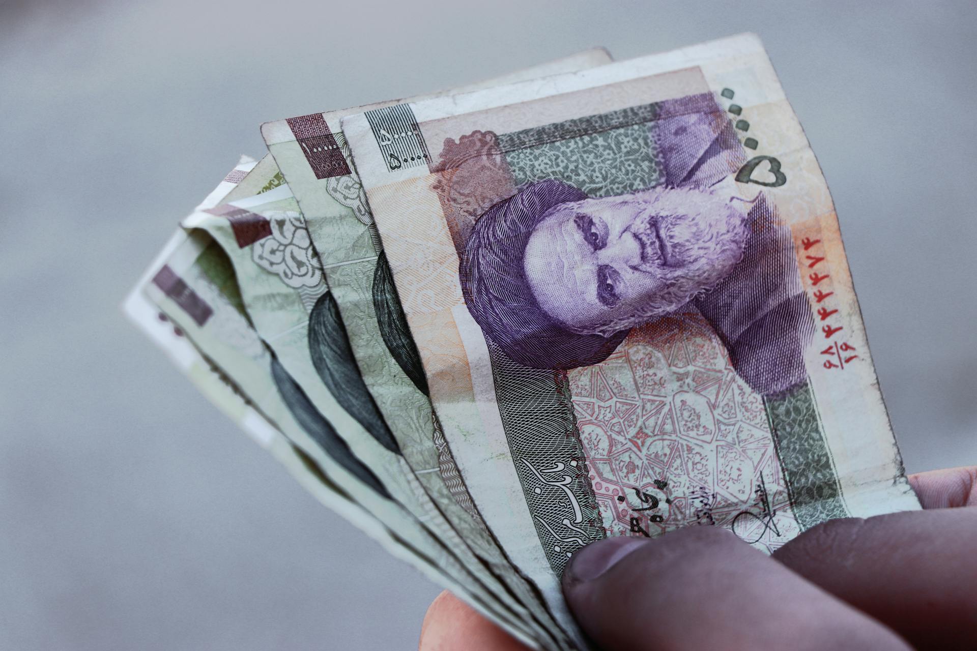 Detailed view of Iranian rial banknotes held in hand, illustrating finance and economy in Iran.