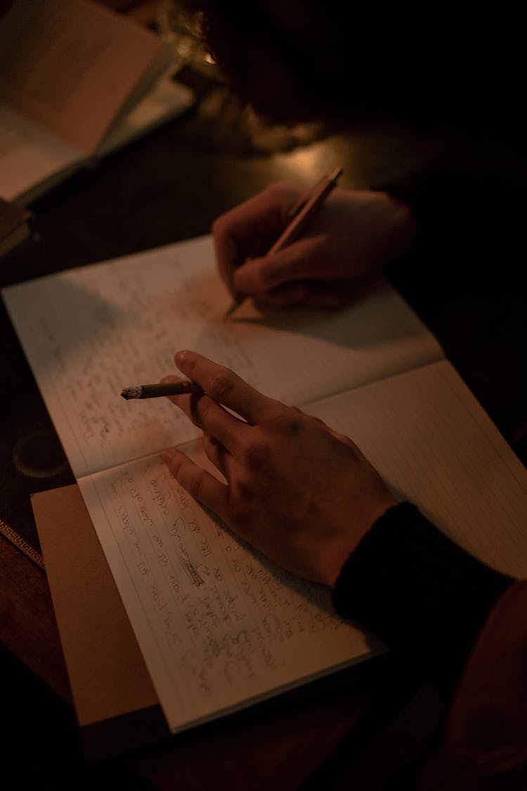 A Person Holding A Cigarette While Writing 