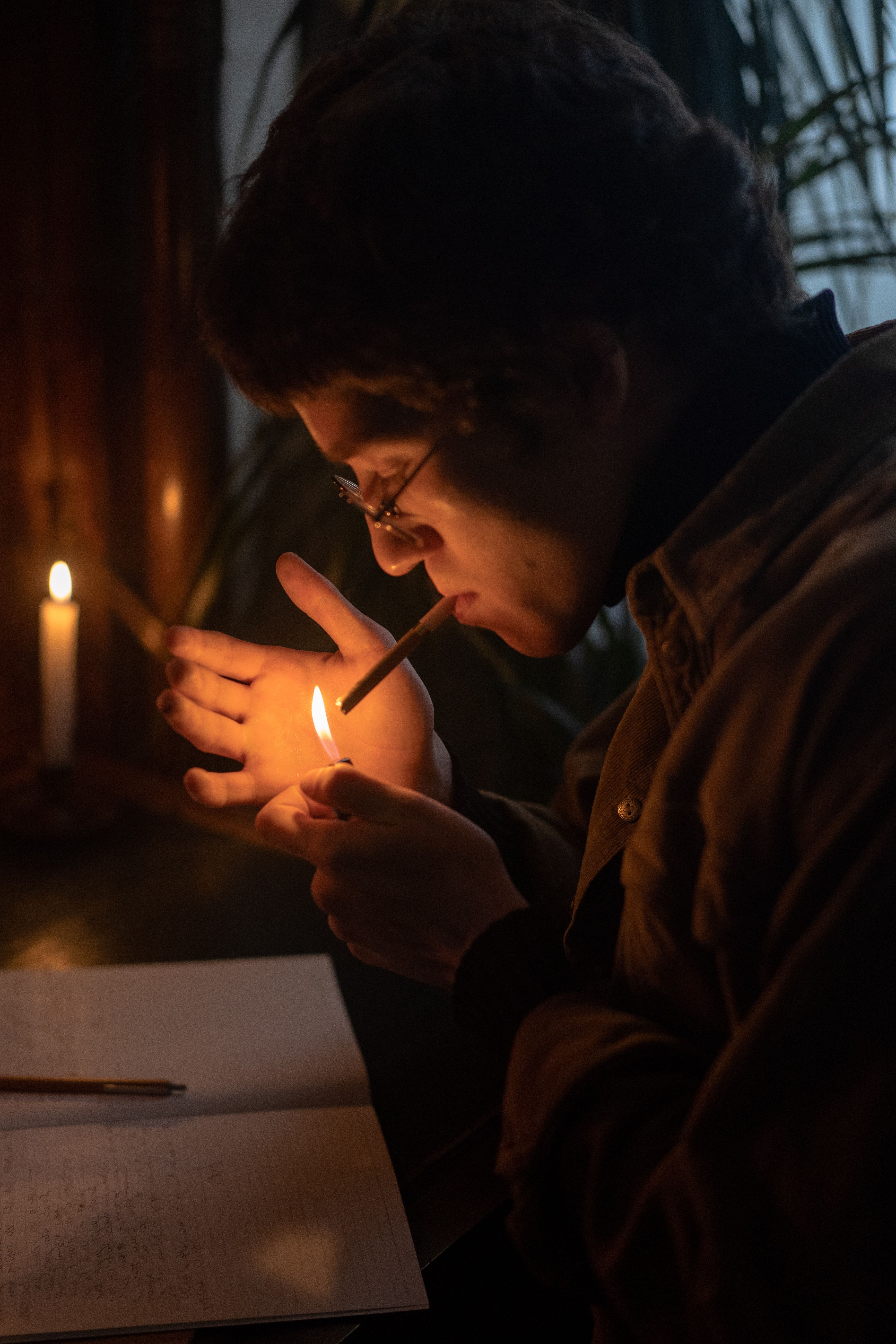An adult male lighting a cigarette indoors beside a candle, creating a warm atmosphere.