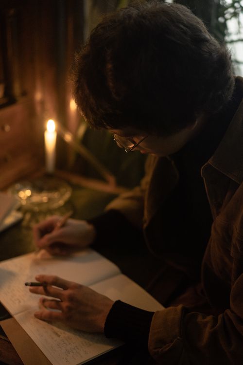 Free Adult writing in a notebook by candlelight, creating a warm and moody ambiance. Stock Photo