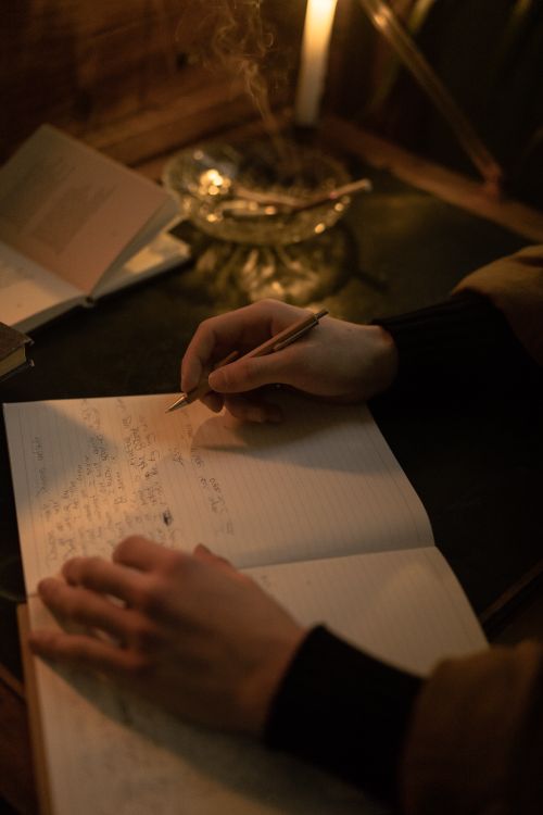Free Person writing in a notebook by candlelight, creating a warm, nostalgic ambiance. Stock Photo