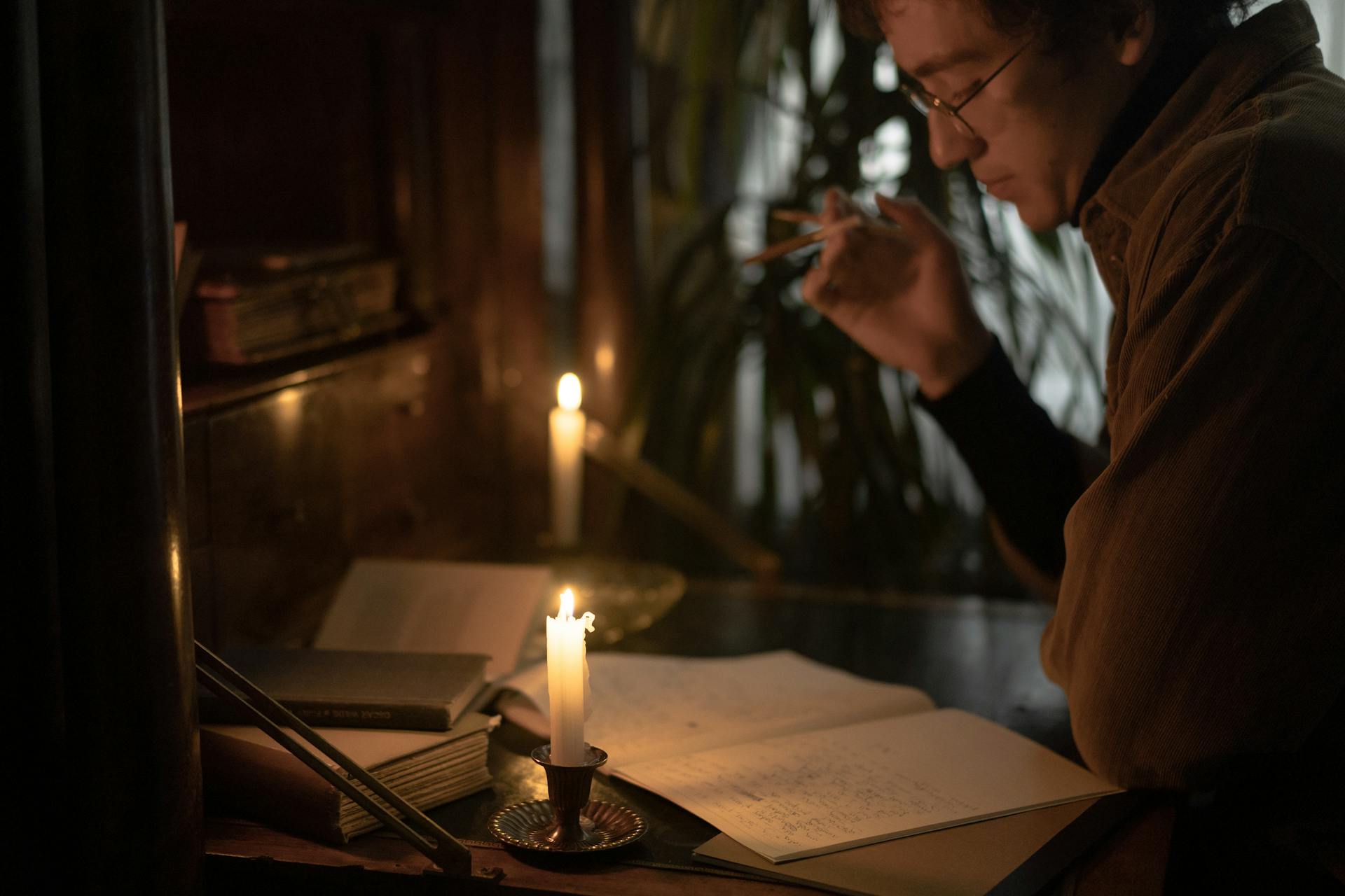 A person reads and writes by candlelight, creating a moody and contemplative atmosphere.