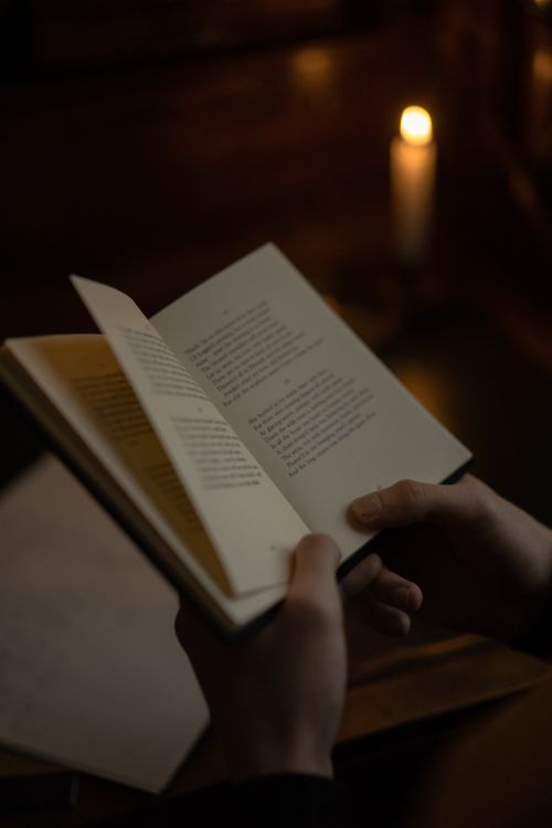 Free Hands holding an open book, reading by candlelight in a dimly lit room, evoking a cozy and contemplative mood. Stock Photo