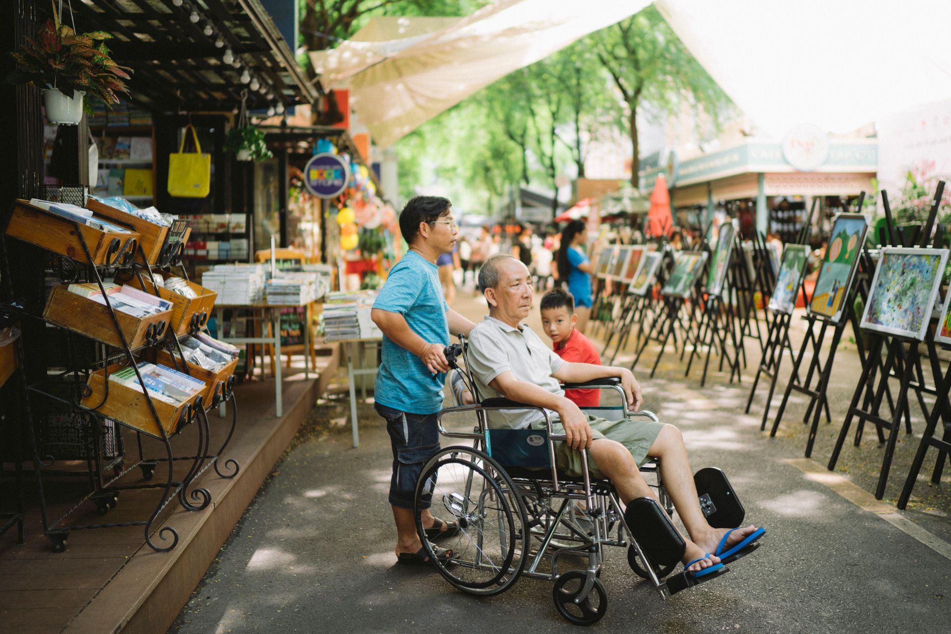 Family explores outdoor art market in Ho Chi Minh City, Vietnam, enjoying paintings and street shopping.