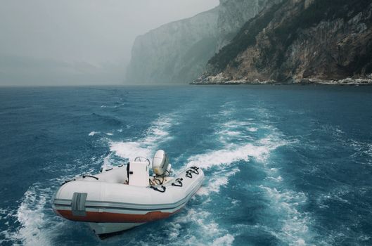 A motorboat creates waves as it navigates the clear blue sea near towering cliffs, capturing the essence of adventure.