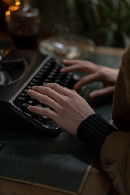 Free Hands of an adult typing on a vintage typewriter, set indoors with classic tones. Stock Photo